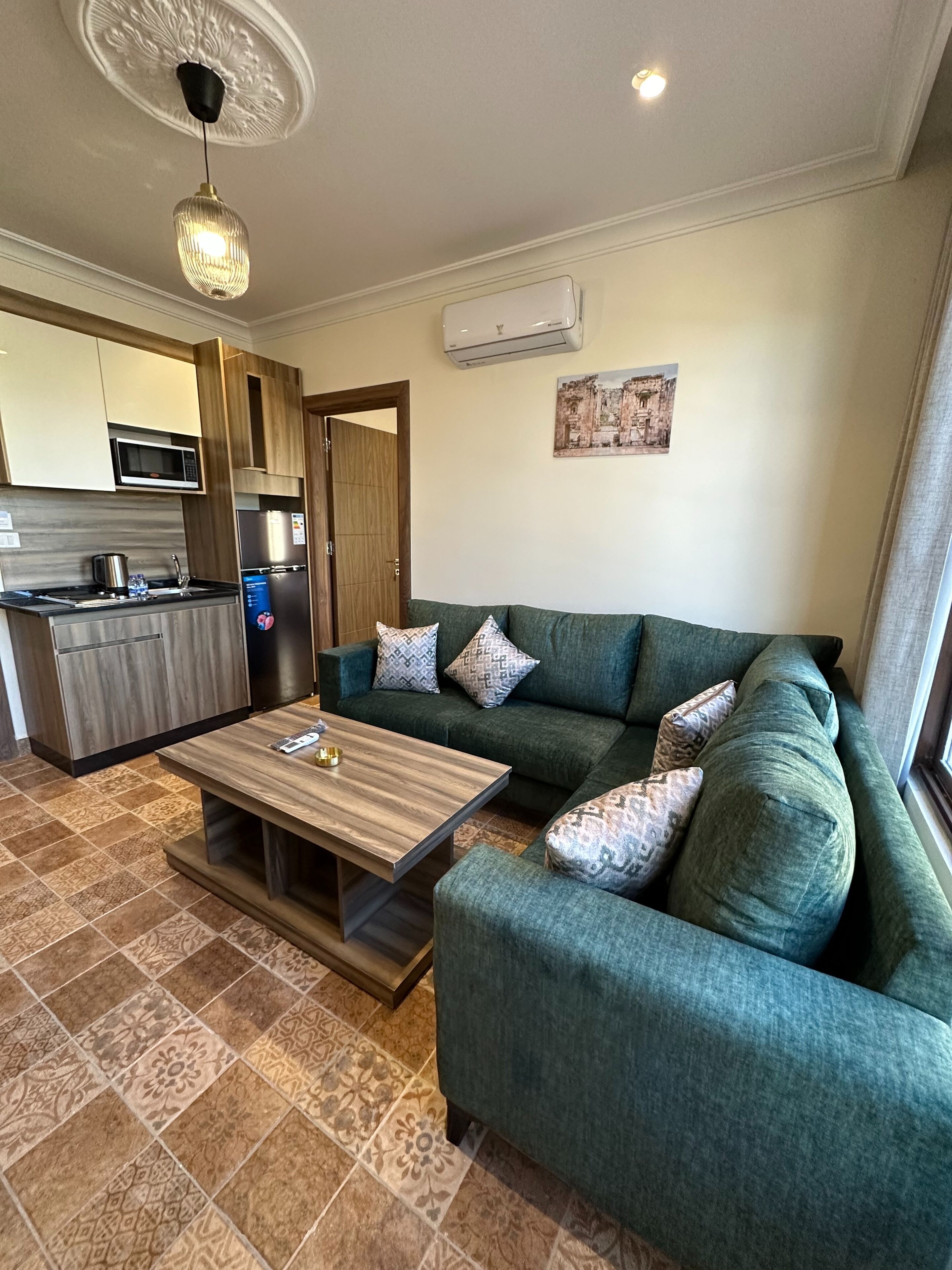 A modern living area with a sofa, coffee table, kitchen with microwave, refrigerator, and decorative ceiling light.