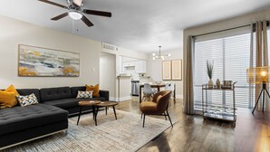A modern living room with a sectional sofa, a coffee table, and a dining area with a chandelier. - Walk to AT&T/Globe Life -Modern 2 Bedroom Retreat (Arlington)