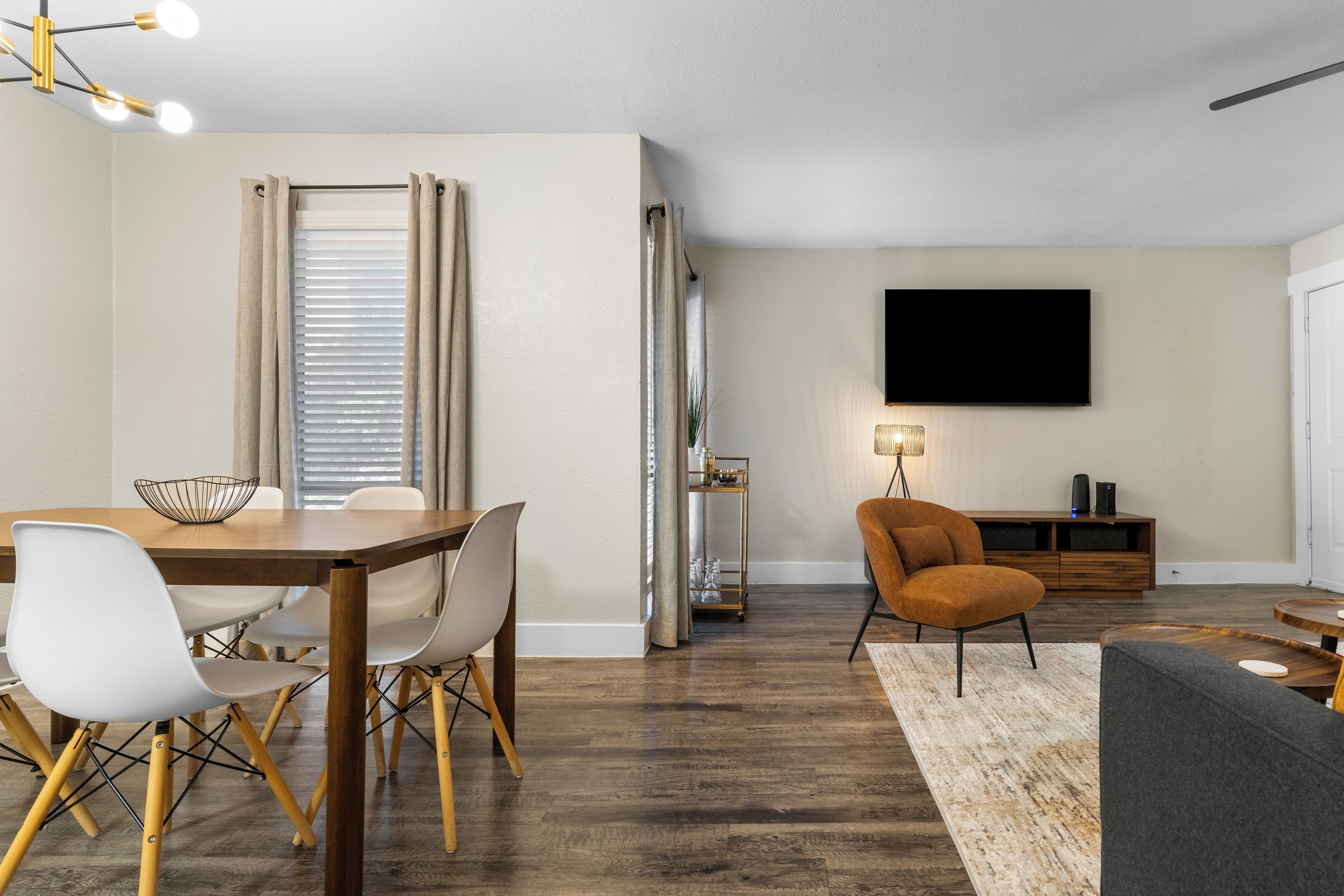 A modern living room with a dining area, wooden flooring, and a flat-screen TV mounted on the wall.