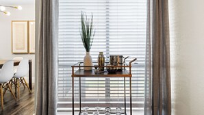A room with a dining area, a window with blinds, a metal tray table with decorative items, and a potted plant. - Walk to AT&T/Globe Life -Modern 2 Bedroom Retreat (Arlington)
