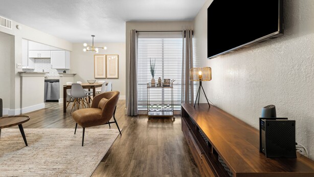 A modern living room with a wooden entertainment unit, a flat-screen TV, and a dining area with a table and chairs. - Walk to AT&T/Globe Life -Modern 2 Bedroom Retreat (Arlington)