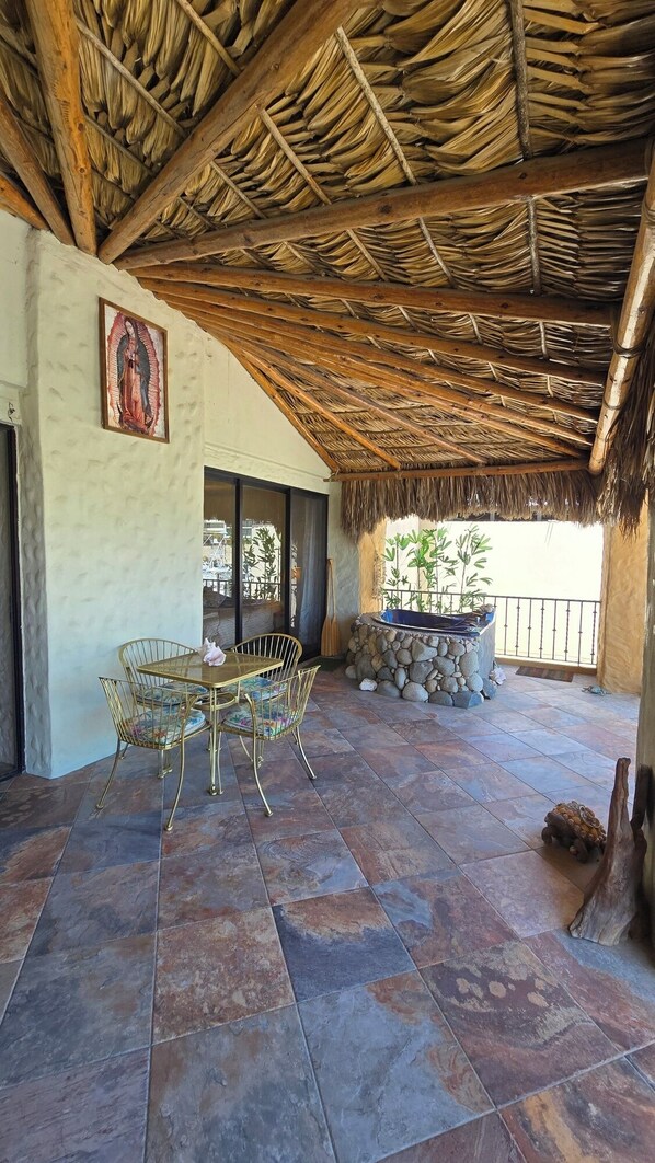 Un patio cubierto con techo de paja, suelo de piedra y un conjunto de asientos.