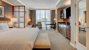 Une chambre d’hôtel avec un grand lit, un bureau, une chaise, une kitchenette et une grande fenêtre.