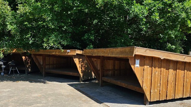 Une rangée de structures en bois, dotées de bancs, probablement destinées à servir d’espaces de repos ou de sièges en plein air.
