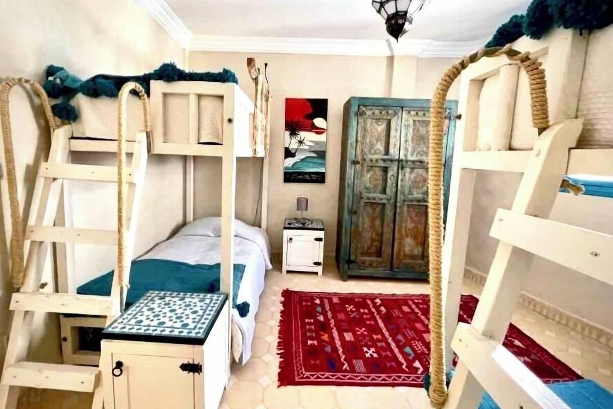 A room with bunk beds, a small table, a cabinet, a red rug, and a wall-mounted shelf with a painting.