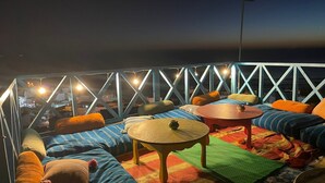 A rooftop terrace with a view of the city at night, featuring a seating area with cushions and a small table. - Taghazout ocean view (Taghazout)