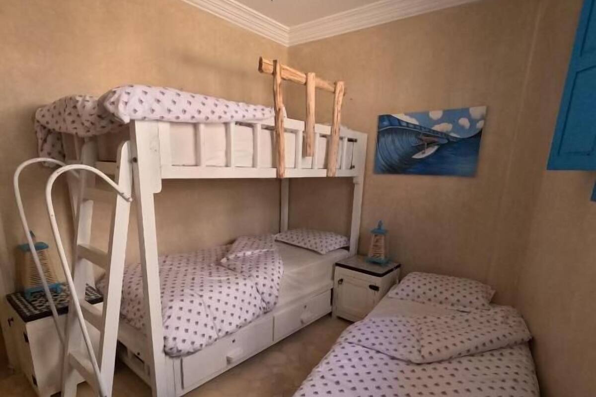 A room with bunk beds, a small bedside table, a nightstand, and a wall painting.