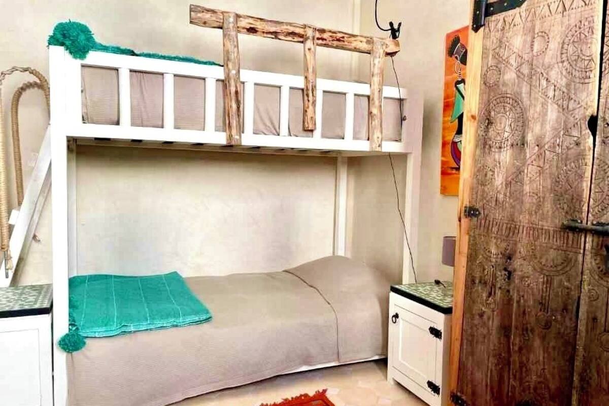 A bunk bed with a wooden ladder, a small bedside table, and a door with intricate carvings.
