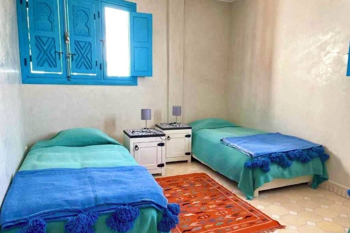 A small, clean room with two beds, a nightstand, and a patterned rug.