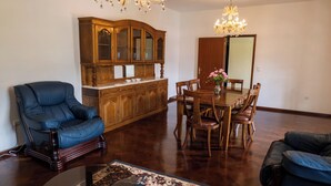 Een woonkamer met een blauwe leren fauteuil, een houten eettafel met stoelen, een houten kast en een kroonluchter.