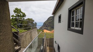 Een balkon met glazen hekwerk met uitzicht op een kustlandschap, met een gebouw en een berg in de verte.