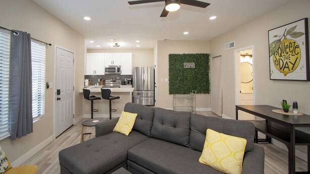 A modern living room with a sectional sofa, a dining area, and a kitchen in the background.