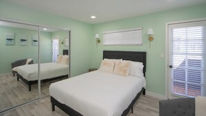 A bedroom with a bed, a mirror, a door, and a window with blinds.
