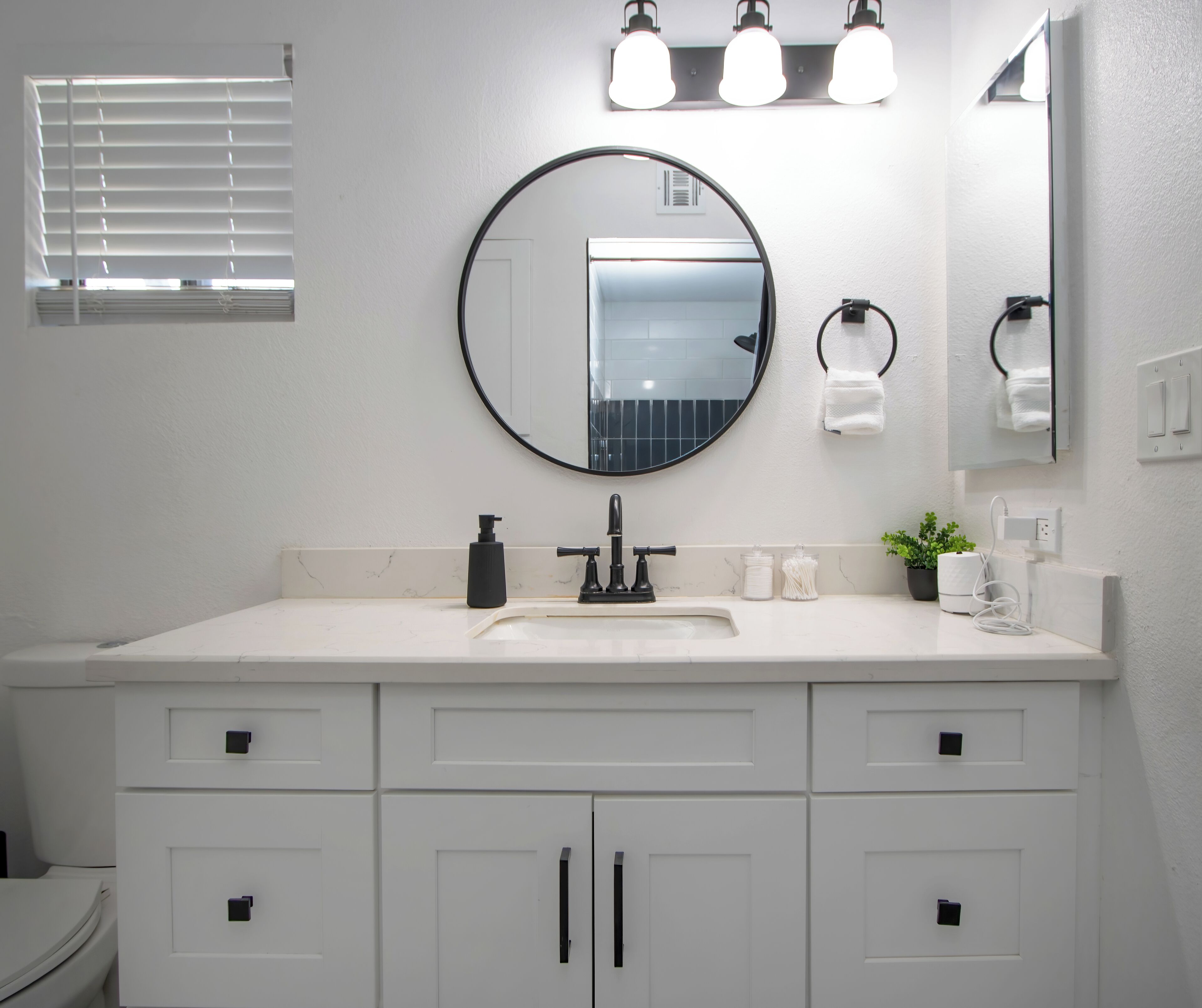 A bathroom with a white vanity, a round mirror, a black faucet, and a towel rack.
