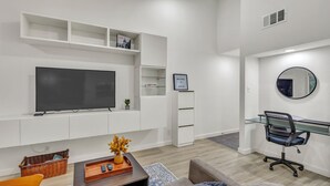 A modern living room with a flat-screen TV, white shelving, a glass desk, and a comfortable seating area. - Newly Renovated Condo - Deck, Pet-Friendly, WFH (Austin)