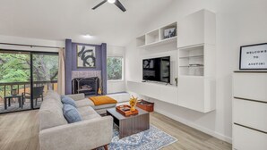 A modern living room with a sofa, coffee table, TV, fireplace, and a balcony with outdoor furniture. - Newly Renovated Condo - Deck, Pet-Friendly, WFH (Austin)