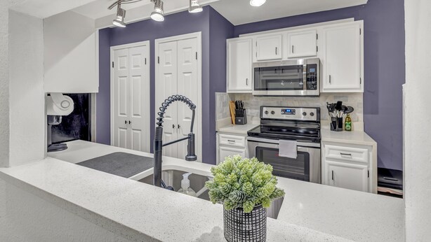 A modern kitchen with white cabinets, a stainless steel microwave, an oven, and a sink with a faucet. - Newly Renovated Condo - Deck, Pet-Friendly, WFH (Austin)