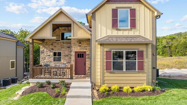 A two-story house with a stone facade, a red door, and a small porch with a railing.