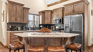 A kitchen with wooden cabinets, a stainless steel refrigerator, and a central island with stools.