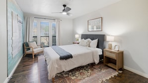 A bedroom with a bed, a chair, a nightstand, a ceiling fan, and a window with blinds.
