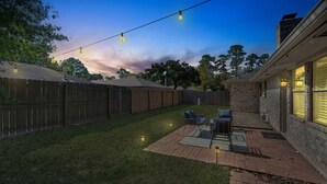 A backyard with a patio area, a wooden fence, and string lights.