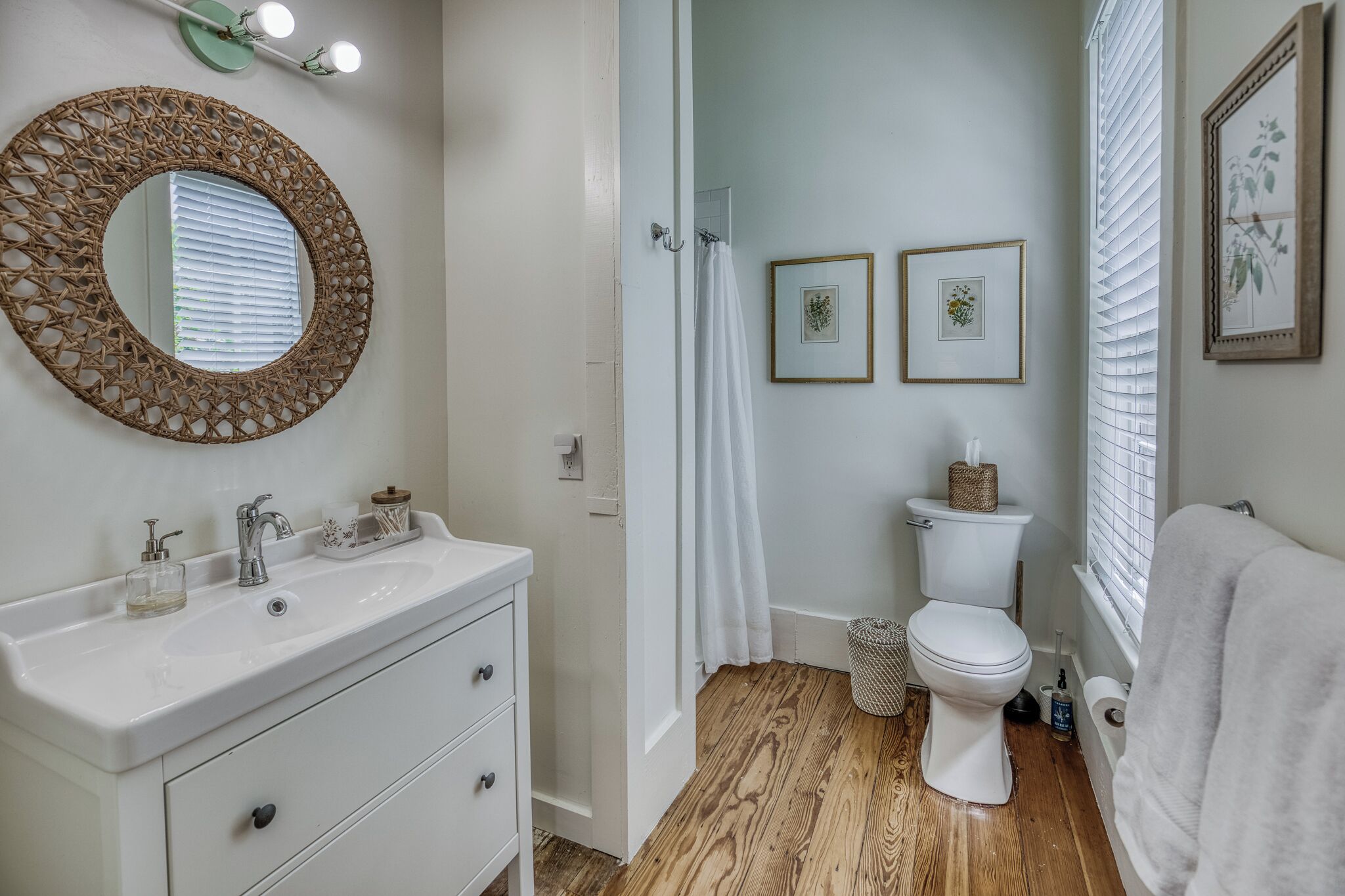 A bathroom with a white sink, a round mirror, a toilet, and framed pictures on the wall.