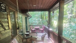 Una terraza de madera con un banco acolchado, sillas de mimbre y una mesa con una jarra y una vela.