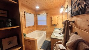 Un baño de cabaña de madera con una bañera, dos lavamanos y un armario de madera.