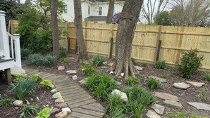 A garden with a wooden pathway, various plants, and a wooden fence. - Dog-friendly 2 bedroom beach bungalow with AC and outdoor fire-pit in Ocean View (Ocean View)