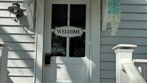 A white door with a 'WELCOME' sign, a mailbox, and a hanging decoration. - Dog-friendly 2 bedroom beach bungalow with AC and outdoor fire-pit in Ocean View (Ocean View)