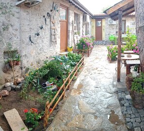 Une cour rustique avec un sol en pierre, une clôture en bois et diverses plantes en pot.
