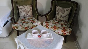 Une pièce comprenant deux fauteuils rembourrés aux motifs floraux, accompagnés de coussins assortis, une petite table sur laquelle se trouve un plateau avec deux tasses et un objet décoratif, et un canapé blanc dont on aperçoit une partie sur la gauche.