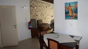 Un coin repas comprenant une table, des chaises, un extincteur et un tableau représentant un voilier.