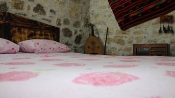 Un dormitorio con pared de piedra, una cama con colcha floral rosa, cabecero de madera, una guitarra y una radio.