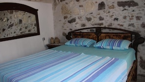 Une chambre avec un mur en pierre, un cadre de lit en bois et une couvre-lit à rayures.