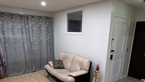 A living room with a beige sofa, a patterned armchair, a small table with a vase, a door, and a window. - Restful Pause on your Journey-14 mins to Airport, 3 beds, 1.5bath up to 6 guests (Calgary)