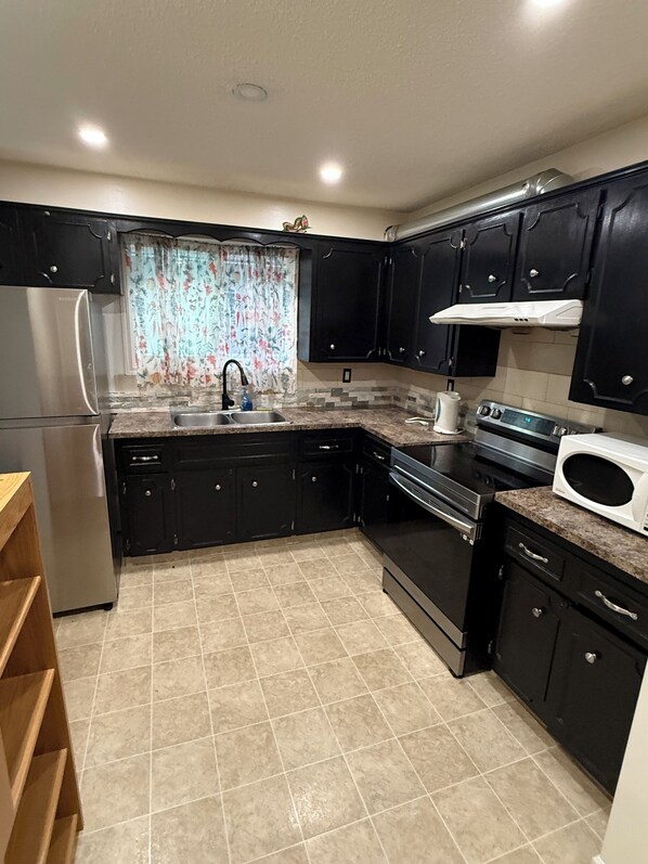 A kitchen with dark cabinets, a stainless steel refrigerator, a sink, a stove, and a microwave.