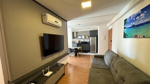 Un salon moderne avec un téléviseur à écran plat, un canapé, un coin repas et une cuisine en arrière-plan.