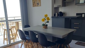 Une cuisine moderne avec des meubles de couleur sombre, un four à micro-ondes et une machine à café. On y trouve un coin repas avec une table blanche et des chaises noires, ainsi qu’un petit vase avec des fleurs jaunes posé sur la table.