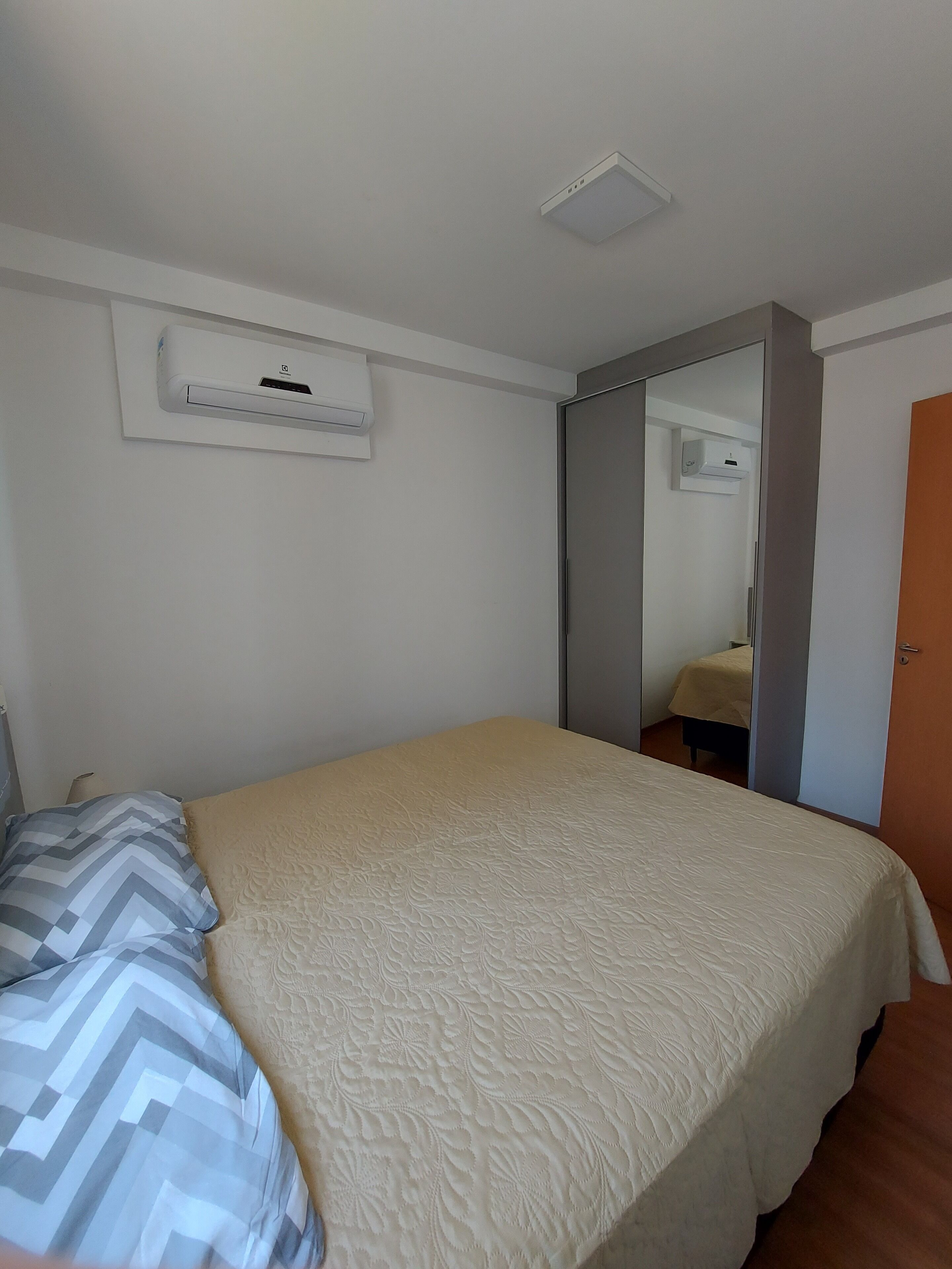 Une chambre à coucher avec un lit, une table de chevet, un miroir et un appareil de climatisation fixé au mur.