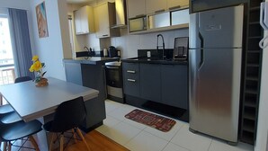Une cuisine moderne avec un plan de travail blanc, des chaises noires et un réfrigérateur en acier inoxydable.