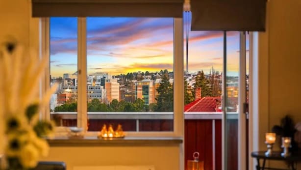 A room with a large window overlooking a cityscape at sunset.