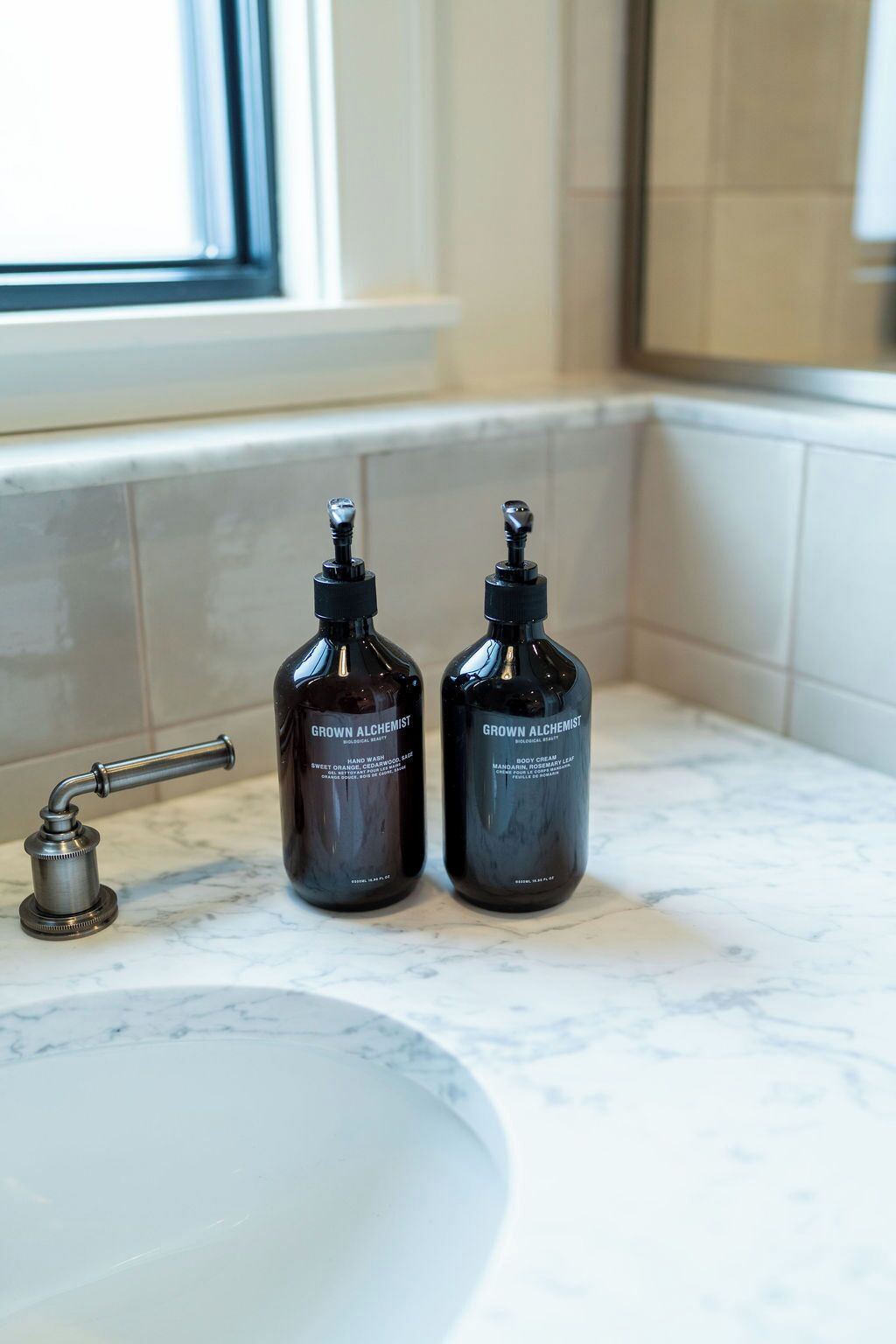 Two dark bottles labeled 'Grown Alchemist' on a bathroom countertop next to a sink.