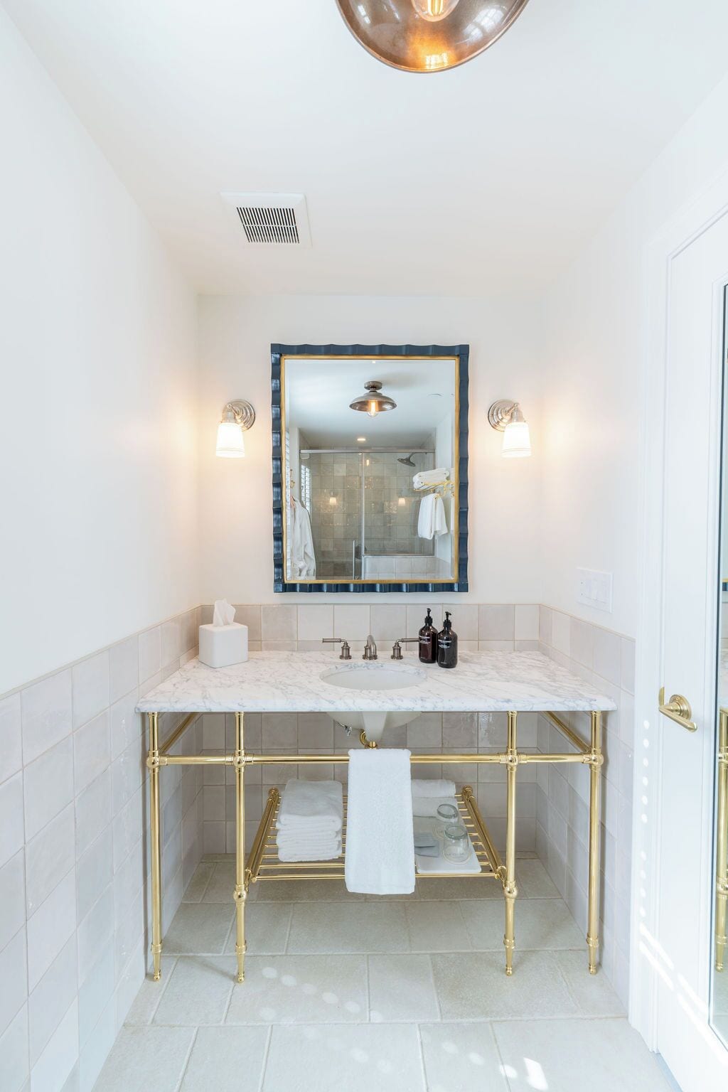 A bathroom with a marble sink, gold fixtures, a glass shower enclosure, and a large mirror with a blue frame.