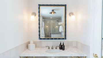 A bathroom with a marble sink, gold fixtures, a glass shower enclosure, and a large mirror with a blue frame.