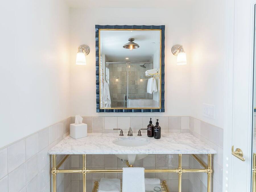 A bathroom with a marble sink, gold fixtures, a glass shower enclosure, and a large mirror with a blue frame.