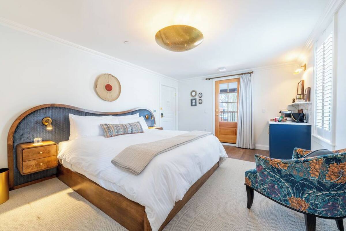 A bedroom with a large bed, a nightstand, a chair, a dresser, and a door with curtains.