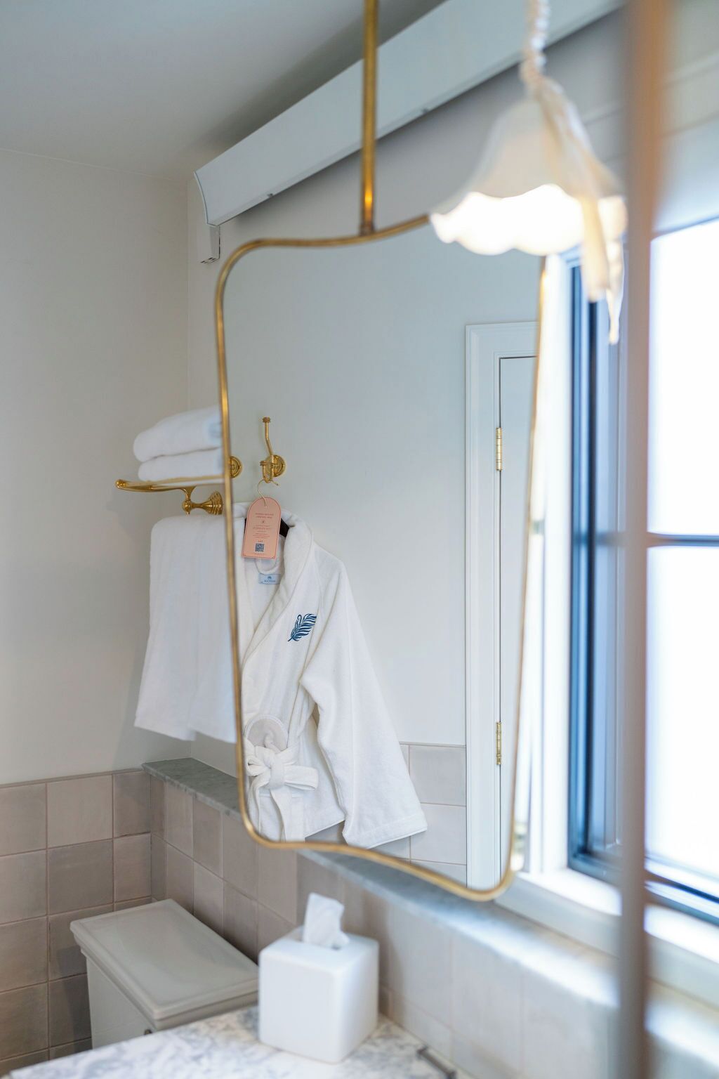 Et badeværelse med et hvidt badekar, et toilet, et håndklædetørrestativ med håndklæder og et spejl med gylden ramme.