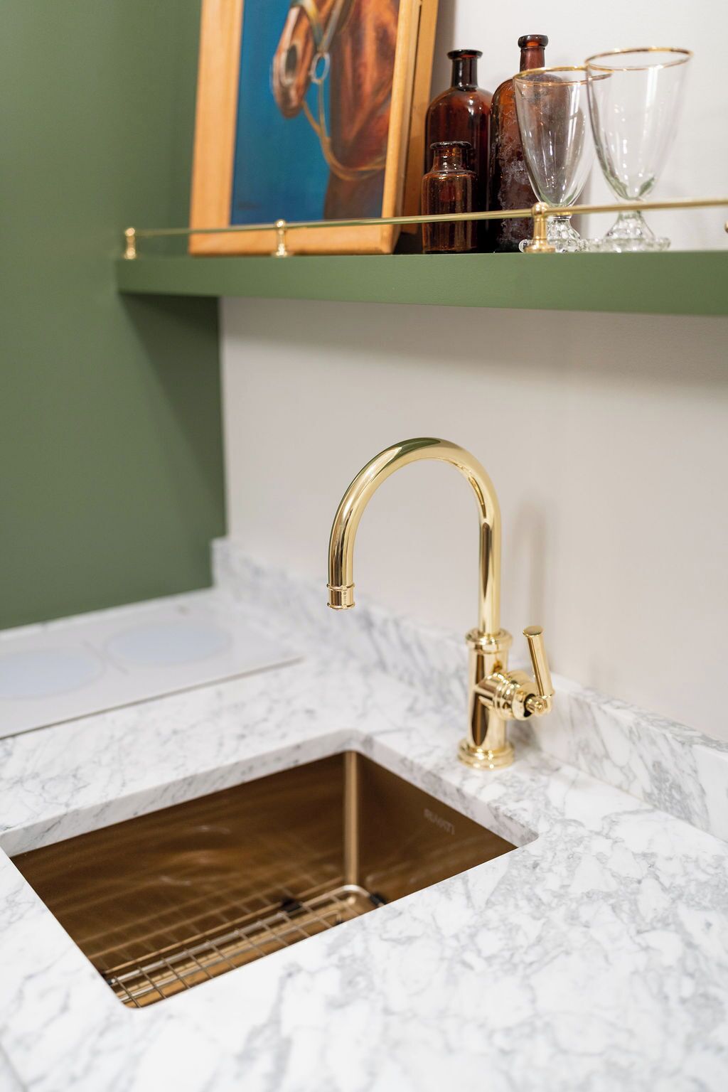 A kitchen with a gold faucet, a marble countertop, and a green shelf above the sink.