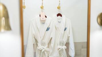A bathroom with two white bathrobes hanging on hooks, a gold-framed mirror, and a white sink with a gold faucet.